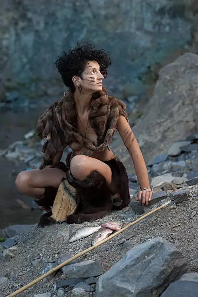 woman dressed as a caveman with captured fish in front of her, looking away