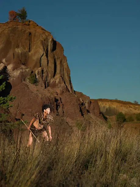 woman dressed as a caveman in nature, holding a spear getting ready to attack