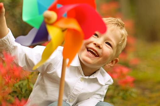 Cheerful little boy is laughing as he is playing with a colorful pinwheel toy. The child is smiling happily as he is playing in the park.