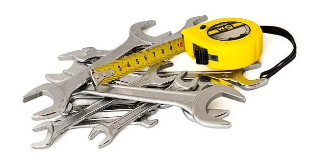 A pile of spanners, wrenches, keys and roulette, tape, tape-measure, tape-line, reel on a white background