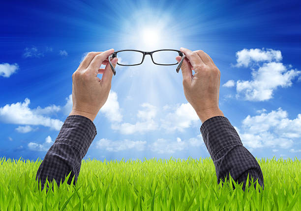 istock Hands holding eyeglasses with blue sky and green field backgroun 472000989