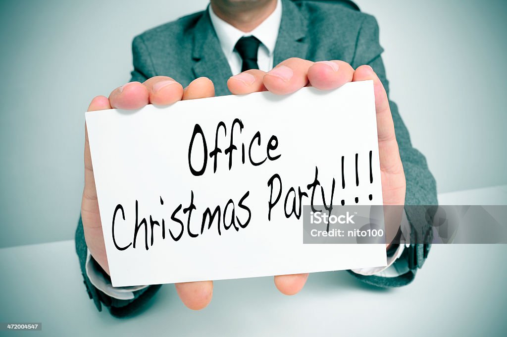 office christmas party a man wearing a suit sitting in a desk holding a signboard with the text office christmas party written in it Adult Stock Photo