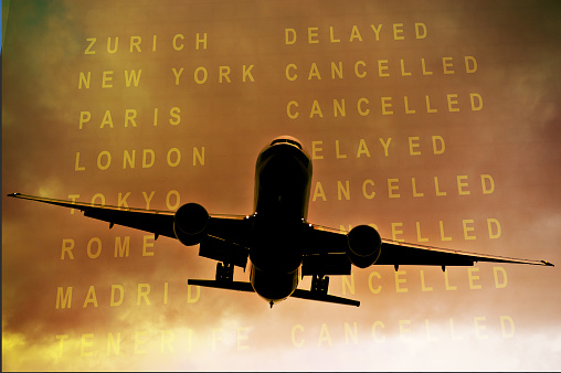 Commercial aircraft airborne against cloudy sky and timetable showing cancelled flights