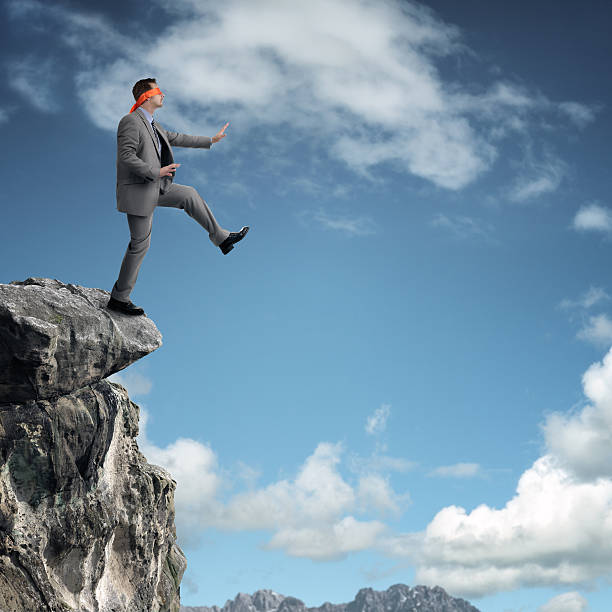 Stepping off a cliff ledge Businessman in a blindfold stepping off a cliff ledge concept for risk, challenge, conquering adversity or ignorance ignorance stock pictures, royalty-free photos & images