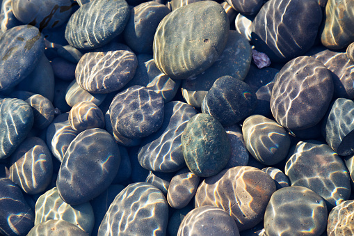 Multicolored pebbles and cobblestones in a stream with sunlight diffraction patterns from surface ripples useful as a background or a texture.