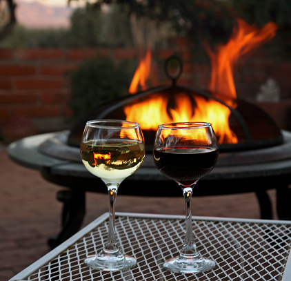 Glass of red and glass of white wine. Chardonnay and Merlot. Evening by the firepit on the patio.
