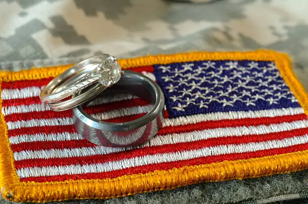 A digital photo of wedding atop the US military flag on an Army uniform creating strong symbolism of military life and strong commitments in marriage and to country.