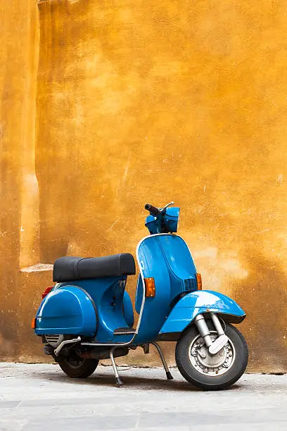 Vintage Blue Scooter Against Yellow Grunge Wall, vertical orientation, Tuscany, Italy