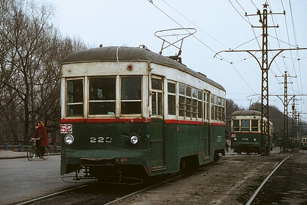 Changchun, China - March 28, 1991: On a cold, gloomy winter day, the driver and some of the passengers at the front of Changchun tram 223 operating on Route 52 are keeping a close watch on the line ahead.  These historic and rather neglected vehicles provided an essential public transport service to the city.  Over time, Changchun has progressively upgraded and expanded its ancient tram system into a modern light rail service.  Two woman cycle alongside the slow moving tram.