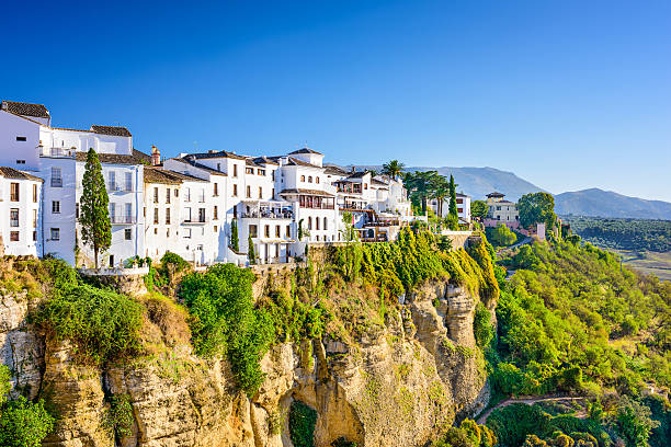 Houses on a cliff in Ronda, Spain surrounded by green trees Ronda, Spain old town cityscape on the Tajo Gorge. andalucia stock pictures, royalty-free photos & images