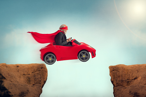 active senior superhero driving a car off a ravine