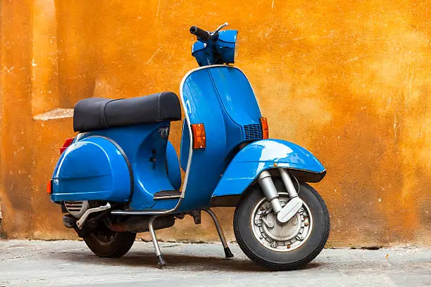Vintage Blue Scooter Against Yellow Grunge Wall, horizontal orientation, Tuscany, Italy