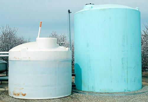 Two plastic storage containers with chemicals such as pesticides near almond orchard in central California