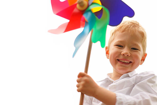 Cheerful little boy is laughing as he is playing with a colorful pinwheel toy. The child is smiling happily. This is an image on a white background with space for text.