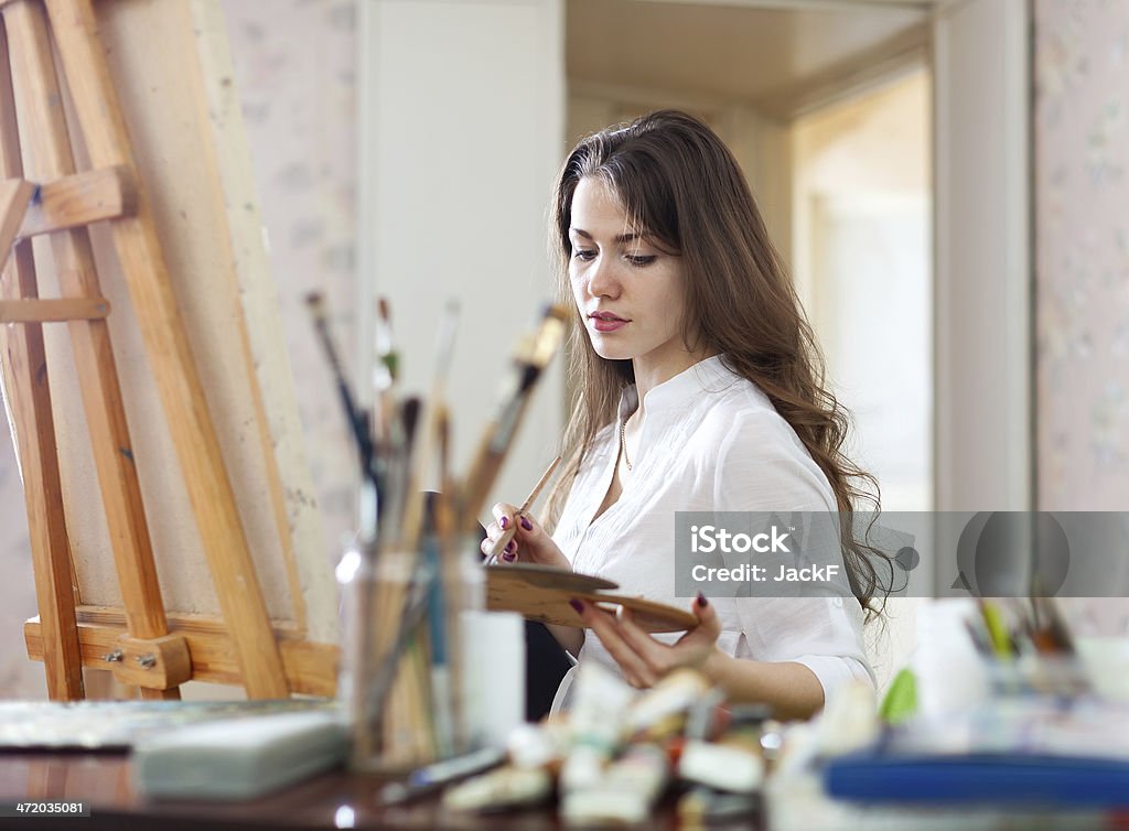 Long-haired woman   paints on canvas Long-haired woman   paints on canvas in workshop interior Adult Stock Photo