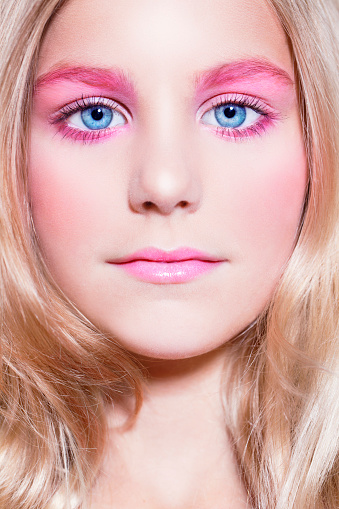 Beautiful young girl looking at the camera with pretty pink make-up, blonde hair.