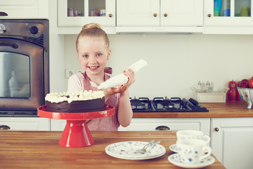 Cute little girl icing a cake in the kitchen