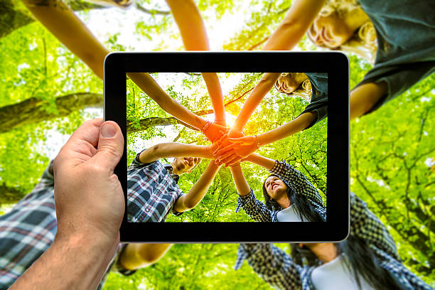 Taking picture from below of Group of friends with hands in hands with sunlight using tablet - Teamwork