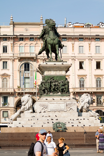 Milan, Italy - September, 1st 2013: Some tourists are standing in front of statue of Vittorio Emanuele II on square Piazza Duomo. A man in forgeround is watching into camera.