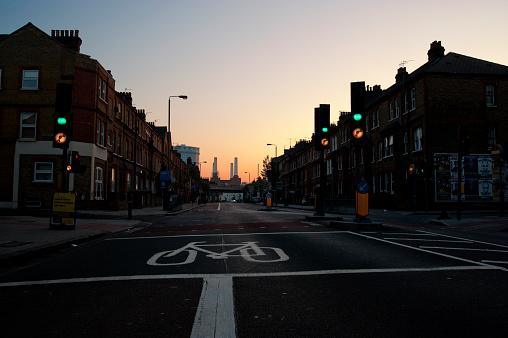 London, England - June 4 2010: Traffic lights and road painted with white lines, showing residential houses in Queenstown Road, Battersea, view of Battersea power station at the end of the road and the sky growing brighter in the dawn