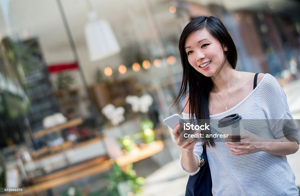 Asian woman walking in the city young Asian woman walking in the city texting on her phone and drinking coffee on the go Chinese Ethnicity Stock Photo