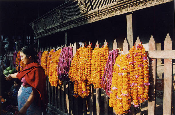 Three clay pots full of colorful flowers with strands of marigolds strewn in front sit on the stone wall at the Mahabodhi temple complex in Bihar, India