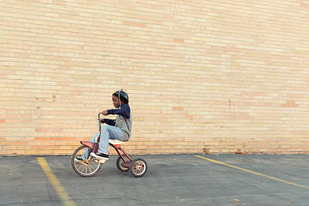 Zoom A young African American boy zips through the city on his tricycle.  big idea stock pictures, royalty-free photos & images