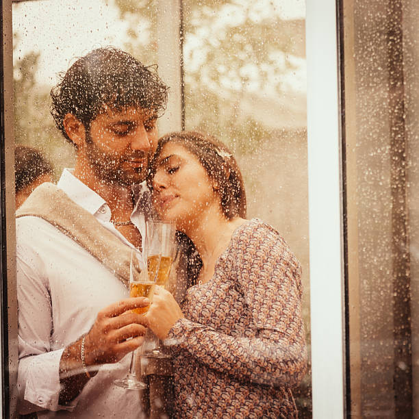 istock Young couple in love behind a wet window drinking champagne 472046549