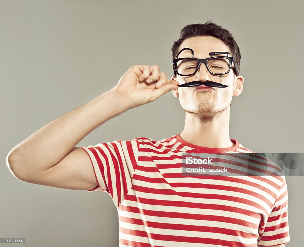 Man wearing face mask Portrait of young man wearing funny face mask and striped t-shirt, curling his mustache. Studio shot. Young Men Stock Photo