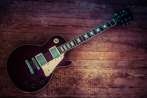 Toledo, Ohio, USA - February 2, 2010: Vintage Les Paul style electic guitar in a deep maroon finish with a distressed hardwood floor in the background.