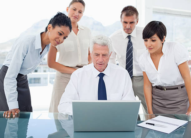 istock Manager working on his laptop with young team around him 472051863