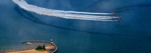Planes Over Water Four planes passing over Lake Michigan during Chicago Air and Water Show, leaving sky trails, casting shadows over the lake, next to beach and breakwater. Extended landscape dimension.  airshow stock pictures, royalty-free photos & images
