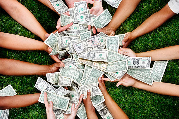 Many hands stretch out to catch or grab a mass of  $1 bills. Grassy background. 