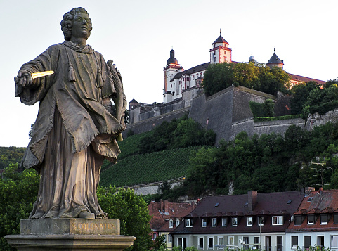 Wuerzburg, Germany - August 4, 2013: Statue of St. Kolonat on the old Main bridge in Wuerzburg. St.Kolonat holding a golden dagger. In the background is the fortress Marienberg the landmark of the city.