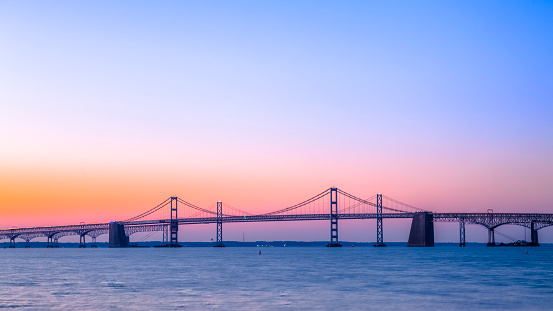A beautiful sunrise over the calm waters under the Chesapeake Bay Bridge. The steel and concrete cantilever and suspension bridge near Baltimore, MD, stretches across the Chesapeake Bay.