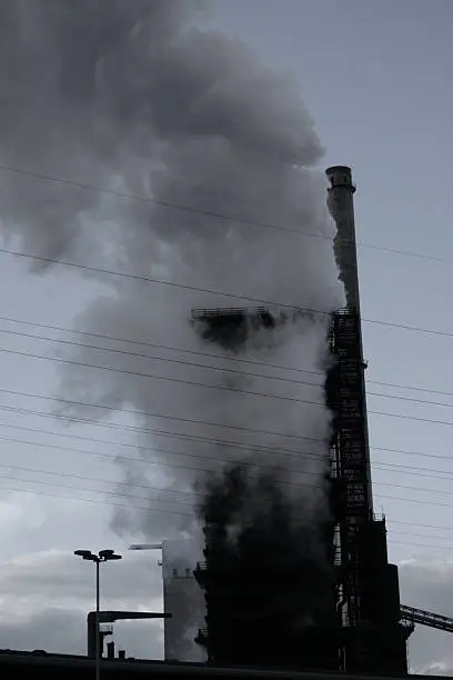 A smaller cooling tower is disappearing in a giant cloud of steam or water vapor as the steel emits from the blast furnace and is cooled on this steel mill