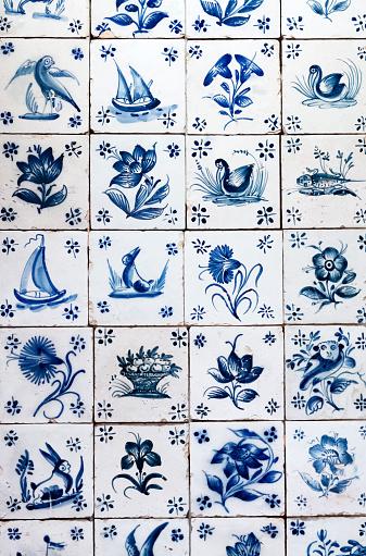 Antique blue & white Delft tile background, with naive symbolic paintings of flowers, animals, birds, and boats.