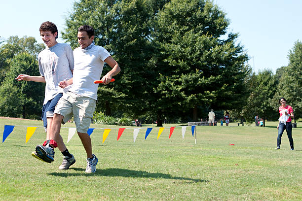 due uomini giovani competono nella corsa a tre gambe in estate raccolta fondi - three legged race foto e immagini stock