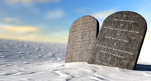 Two stone tablets with the ten commandments inscribed on them standing in brown desert sand infront of a blue sky