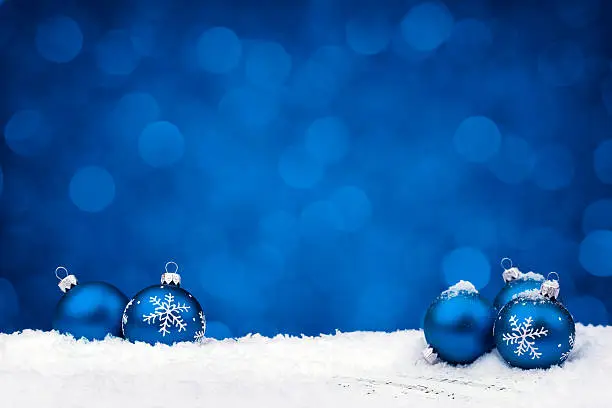 Blue decorated with snowflake baubles lying on snow and sheet notes with christmas carols (Silent Night by F.Gruber 19th c, adante speed), nice christmas lights blue background