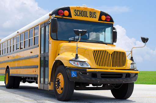 A multiracial group of elementary age boys and girls smile and wave out open windows of a parked yellow school bus on a sunny spring day in the Pacific Northwest region of the United States.