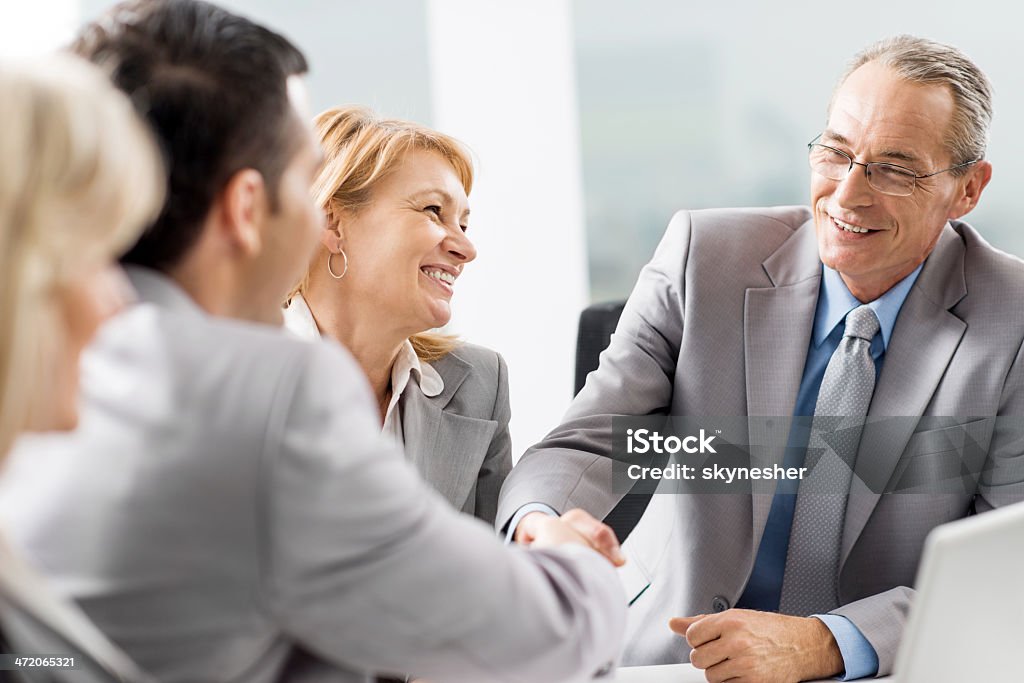 Business people shaking hands. Happy mature businessman shaking hands with his mid adult colleague. Their women colleagues are beside them.    30-39 Years Stock Photo