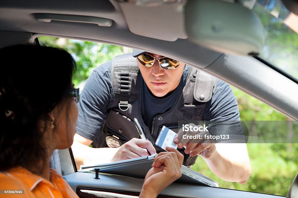 Crime: Policeman gives driver a traffic ticket. Policeman stops woman driver to give her a traffic ticket for speeding.  He takes her driver's license.  Driver's License Stock Photo
