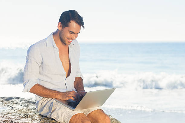 istock Handsome man sitting on a rock using his laptop 472070515