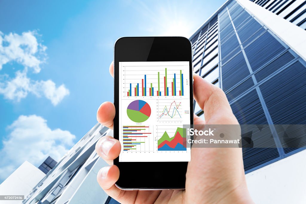 Hand holding phone with graphics against a tall building hand holding mobile phone with analyzing graph against office buildings with sun 2015 Stock Photo