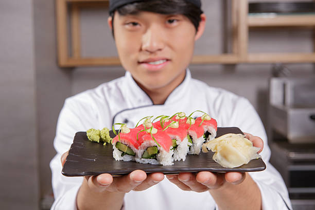 Here is your meal. Closeup of a rectangular plate with tuna sushi with avocado, hazel sauce and seaweed served with wasabi and ginger in focus