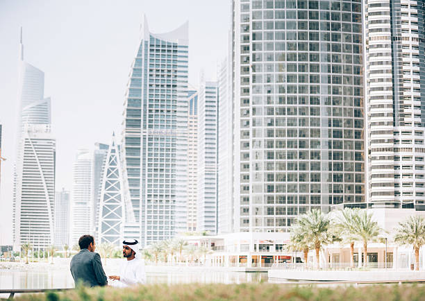 Business outdoors meeting between emirati man and western businessman. They are staying in front of beautiful contemporary background and talking to each other.