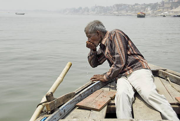 Indian boatman drinks water from Ganges River in Varanasi, India. stock photo