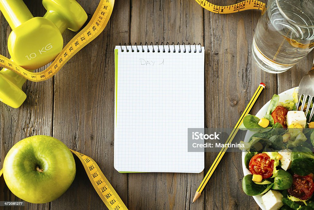 Fitness and healthy food lifestyle concept Workout and fitness dieting copy space diary. Healthy lifestyle concept. Salad, apple, dumbbell, water and measuring tape on rustic wooden table. Healthy Eating Stock Photo