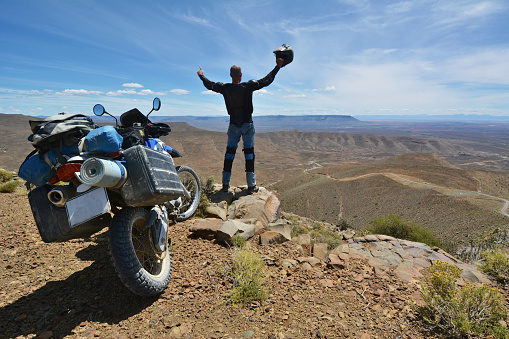 motorcyclist stands next to his motorcycle and appreciates the view over the karoo, south africa